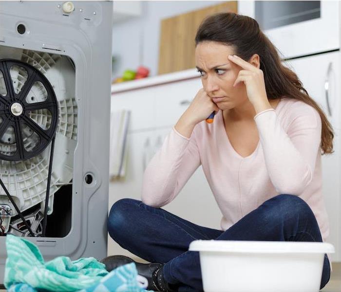 fustrated woman on floor looking at broken washer 